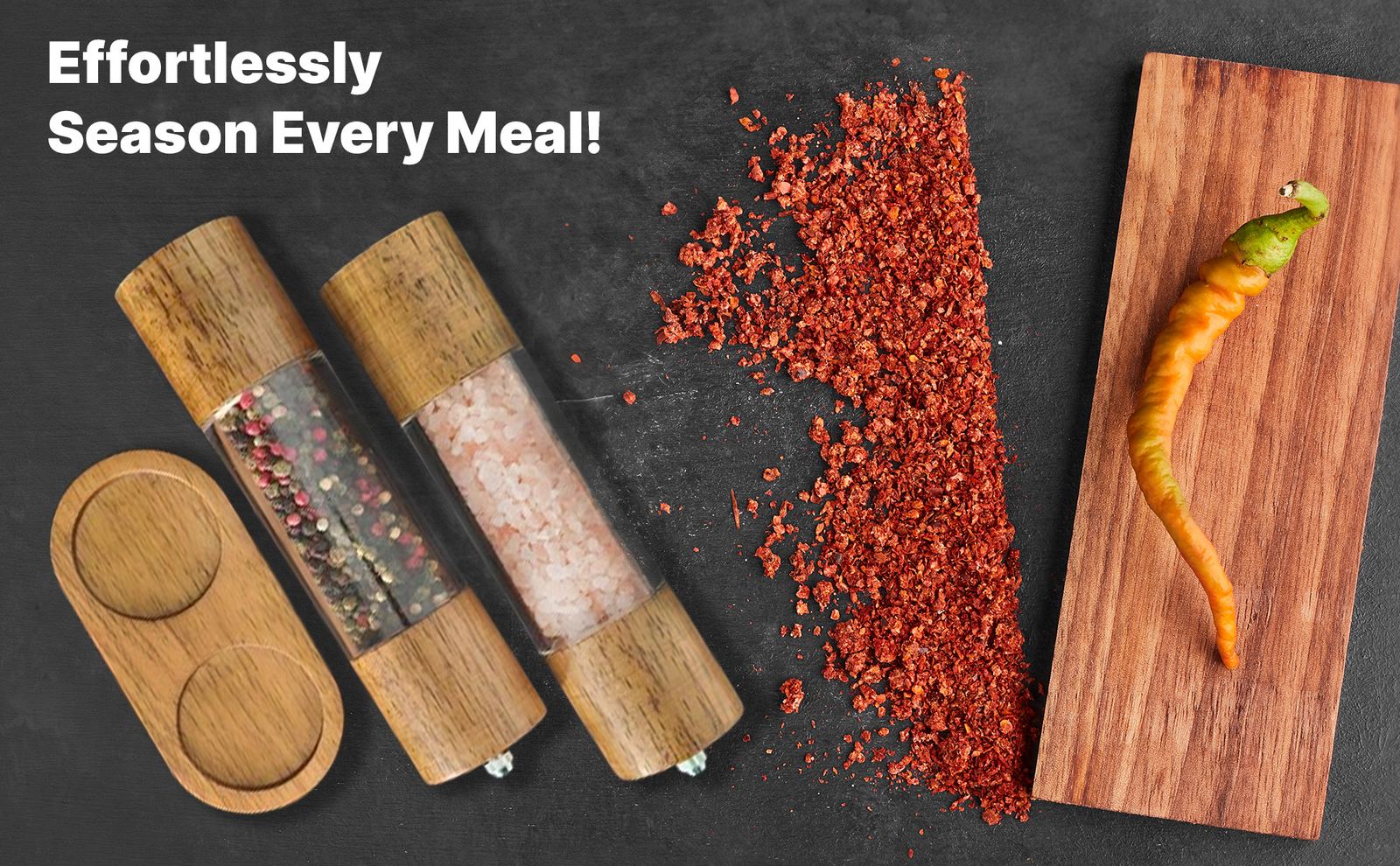 Both grinders and the tray laid flat next to chili flakes and a pepper on a wooden board