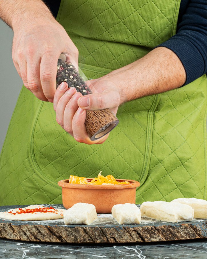 Cook in a green apron grinding pepper over dough and cheese