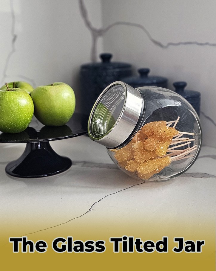 Glass tilted jar filled with rock candy on a marble counter beside green apples