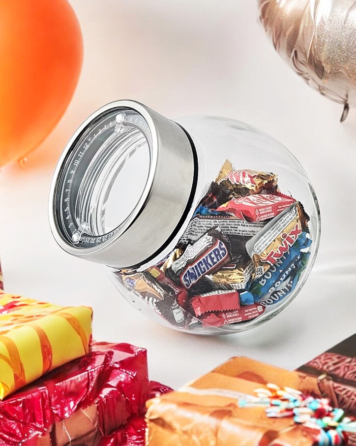 Glass tilted jar filled with chocolates among wrapped gifts and balloons