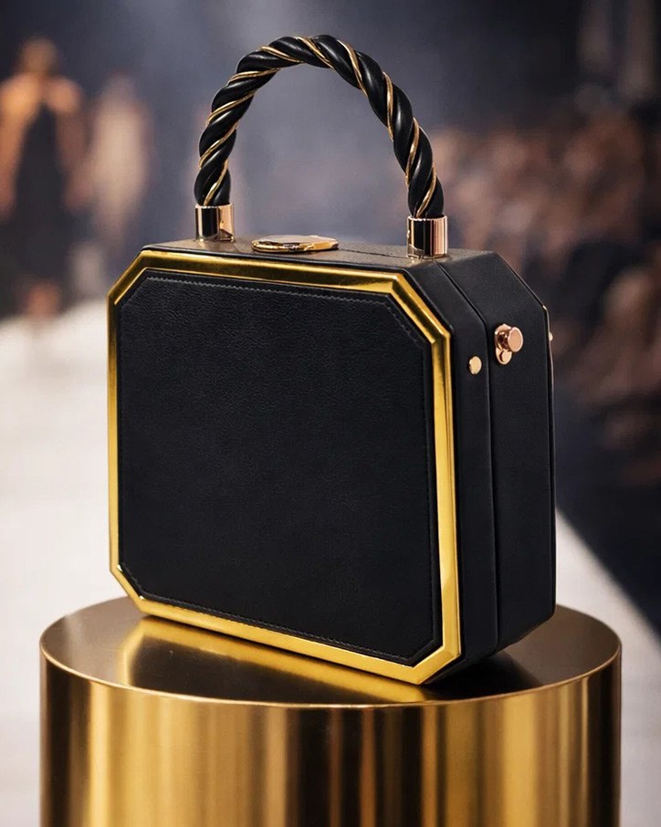 Black Rylique handbag on a gold pedestal under warm spotlights