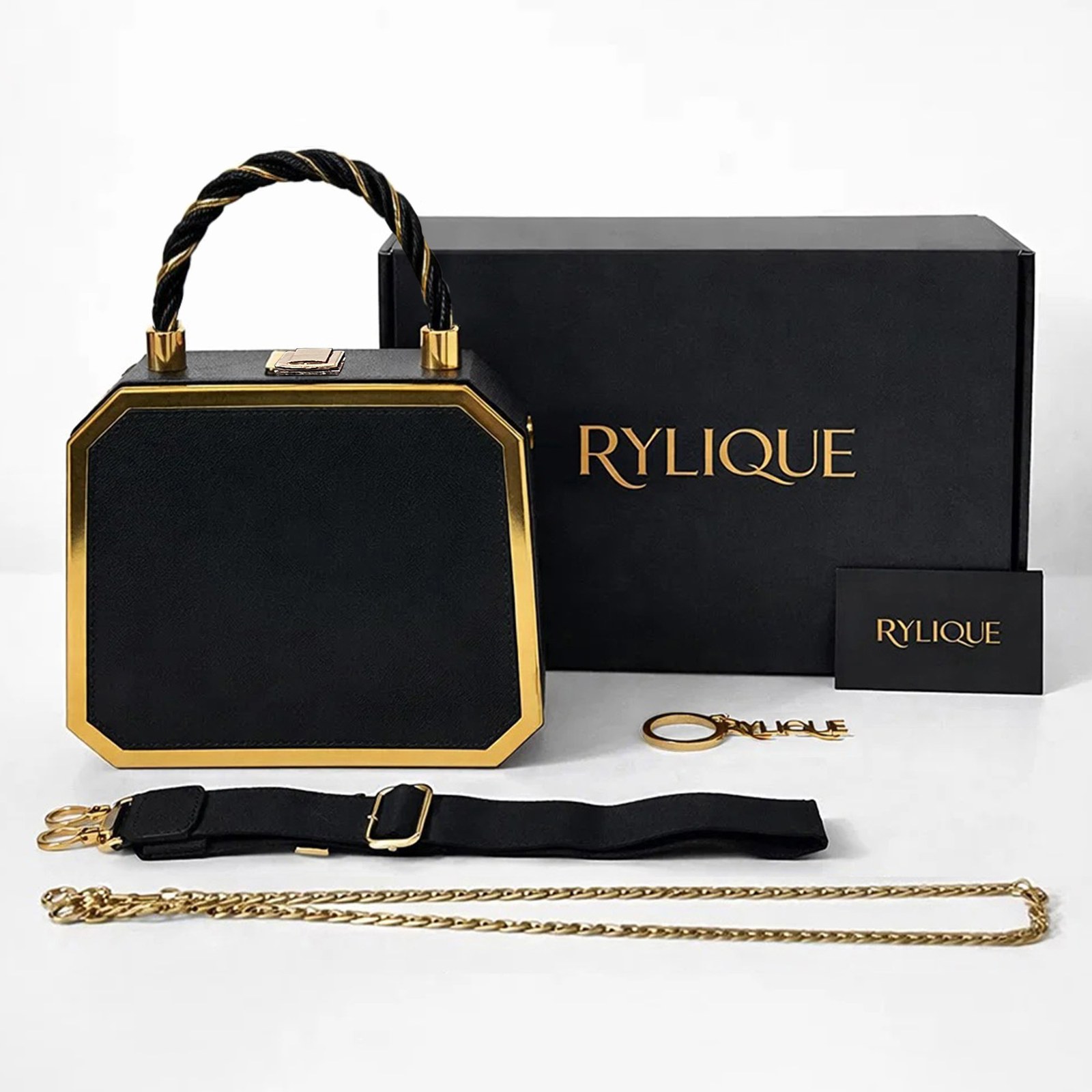 Black octagonal Rylique handbag with a twisted top handle, a black gift box, a webbing strap, a gold chain and a keychain on white