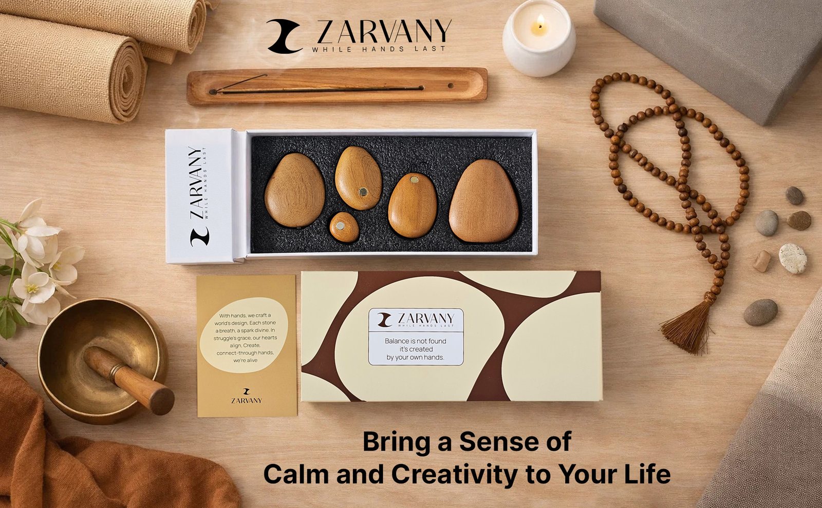Flat lay of wooden stones, the cream and brown box, incense, and prayer beads on a wooden table